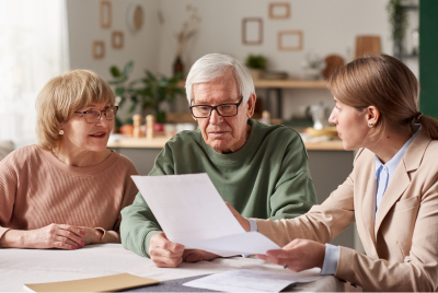 two elderly people sitting next to a women who is showing them paperwork