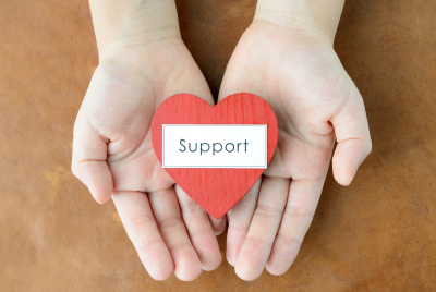 a hand holding a paper heart that says "support'